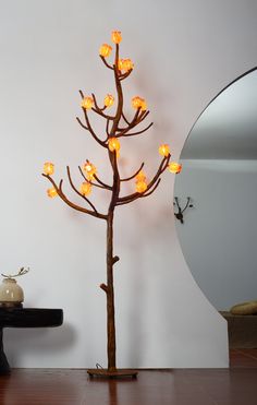 a small tree with lights on it in front of a white wall and mirror next to a black table