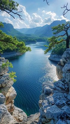 a lake surrounded by rocks and trees with mountains in the background