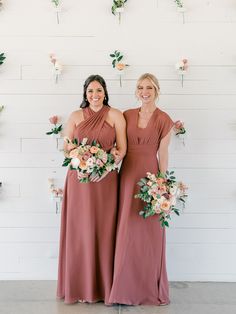 two bridesmaids standing in front of a wall with flowers