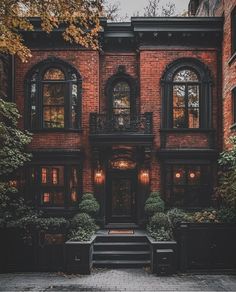 an old brick building with many windows and steps leading up to the front door is lit by lanterns