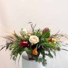 a vase filled with flowers and greenery on top of a white table next to a wall