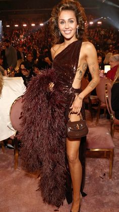 a woman standing in front of a crowd wearing a brown dress and holding a purse