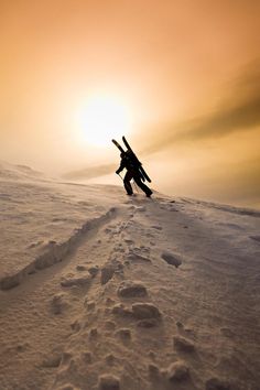 a snowboarder is going down a snowy hill with the sun in the background