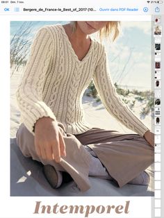 a woman sitting in the sand wearing a sweater and pants