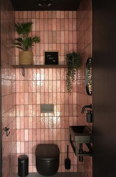 a bathroom with pink tiles and plants on the shelf above the toilet, as well as a black sink