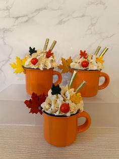 three orange mugs filled with whipped cream and toppings on top of each other