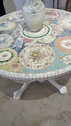 a white vase sitting on top of a table covered in colorful tiles and glass mosaics