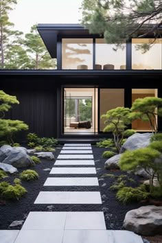 a modern house in the woods with rocks and trees on each side, along with a stone path leading to the front door