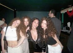 four young women posing for the camera in front of a group of people at a party