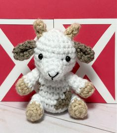 a crocheted sheep sitting in front of a red and white wall with a flag