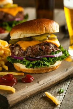 a cheeseburger with fries and ketchup on a cutting board next to a glass of beer