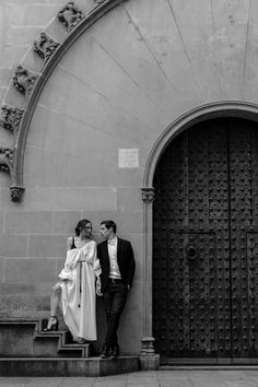 a man and woman standing next to each other in front of a building with large doors