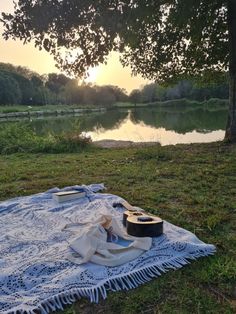 an open guitar case sitting on top of a blanket next to a lake at sunset