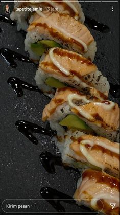 several sushi rolls on a black plate with sauce drizzled over them