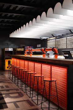 an empty bar with orange bars and stools in front of the counter, under lights