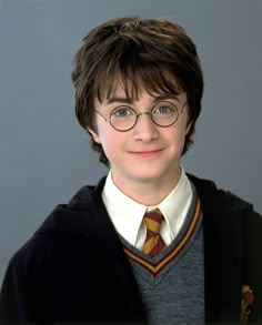 a young boy wearing glasses and a harry potter sweater is smiling for the camera in front of a gray background