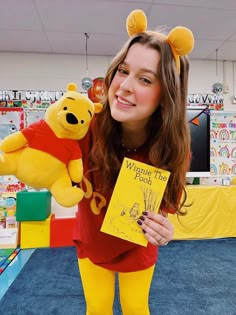 a girl in winnie the pooh costume holding up a book and stuffed animal bear