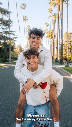 two young men riding on the back of a skateboard in front of palm trees