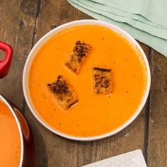 there is a bowl of soup with croutons in it on the wooden table