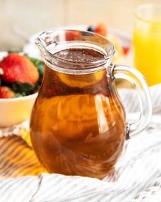 a glass pitcher filled with liquid sitting on top of a table next to a bowl of fruit