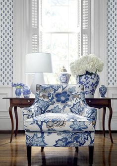 a blue and white chair sitting in front of a window next to a table with flowers