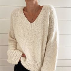 a woman standing in front of a white wall with her hands on her hips wearing a sweater and black pants