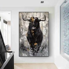 the painting is hanging on the wall next to the stair case in the hallway, and it has a black bull with yellow spots