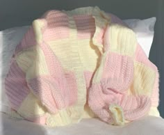 a pink and yellow knitted blanket sitting on top of a bed next to pillows