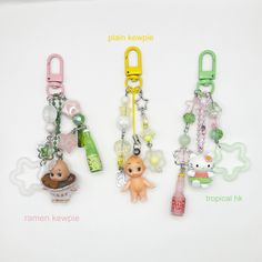 three key chains with charms attached to them on a white surface, one has a baby doll and the other is a bottle opener