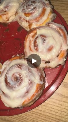 a red plate topped with cinnamon rolls covered in icing