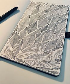 a notebook with an intricate design on the cover and pen next to it, sitting on a table