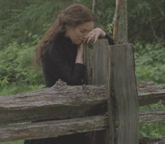 a woman leaning on a wooden fence in the woods