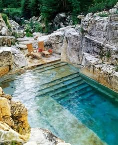 an outdoor swimming pool surrounded by rocks and water features two lawn chairs on the edge