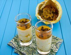 two glasses filled with dessert sitting on top of a blue table next to an open fruit