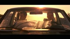 two men are sitting in the back seat of a car as the sun goes down