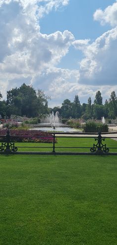 there is a fountain in the middle of this grassy area with benches and flowers around it