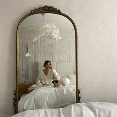 a woman sitting on a bed with her dog in front of a large gold mirror