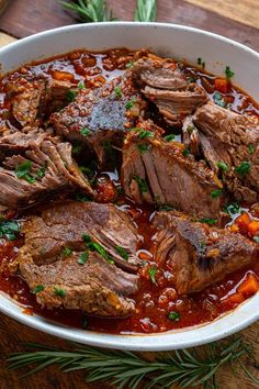 a white bowl filled with meat and tomato sauce on top of a wooden cutting board