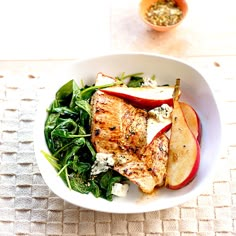 a white bowl filled with chicken, apples and spinach salad on top of a table