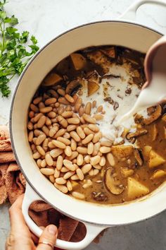 someone pouring milk into a pot filled with beans