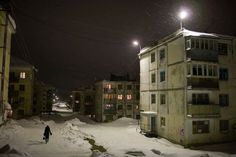 a person walking down a snow covered street in front of apartment buildings at night time