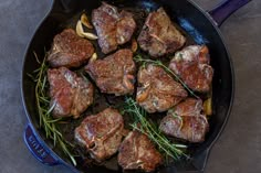 steaks are cooking in a skillet on the stove top, with rosemary sprigs