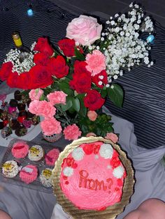 a person holding up a cake with flowers in the background on a table filled with cupcakes