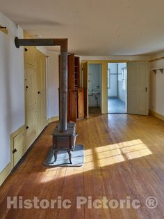 an empty room with wood floors and a stove in the center, surrounded by white walls