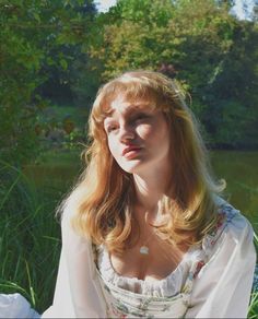 a woman sitting in the grass with her eyes closed and looking off into the distance