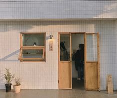 two people standing in the doorway of a white building with wooden doors and window frames