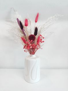 a white vase with red flowers and feathers in it