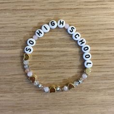 a white and gold beaded bracelet with the word school spelled in small letters on it