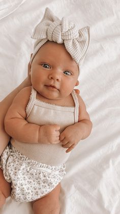 a baby is laying on a white sheet and wearing a knitted bow headband