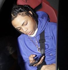 a young man sitting in a car looking at his cell phone while wearing a blue hoodie